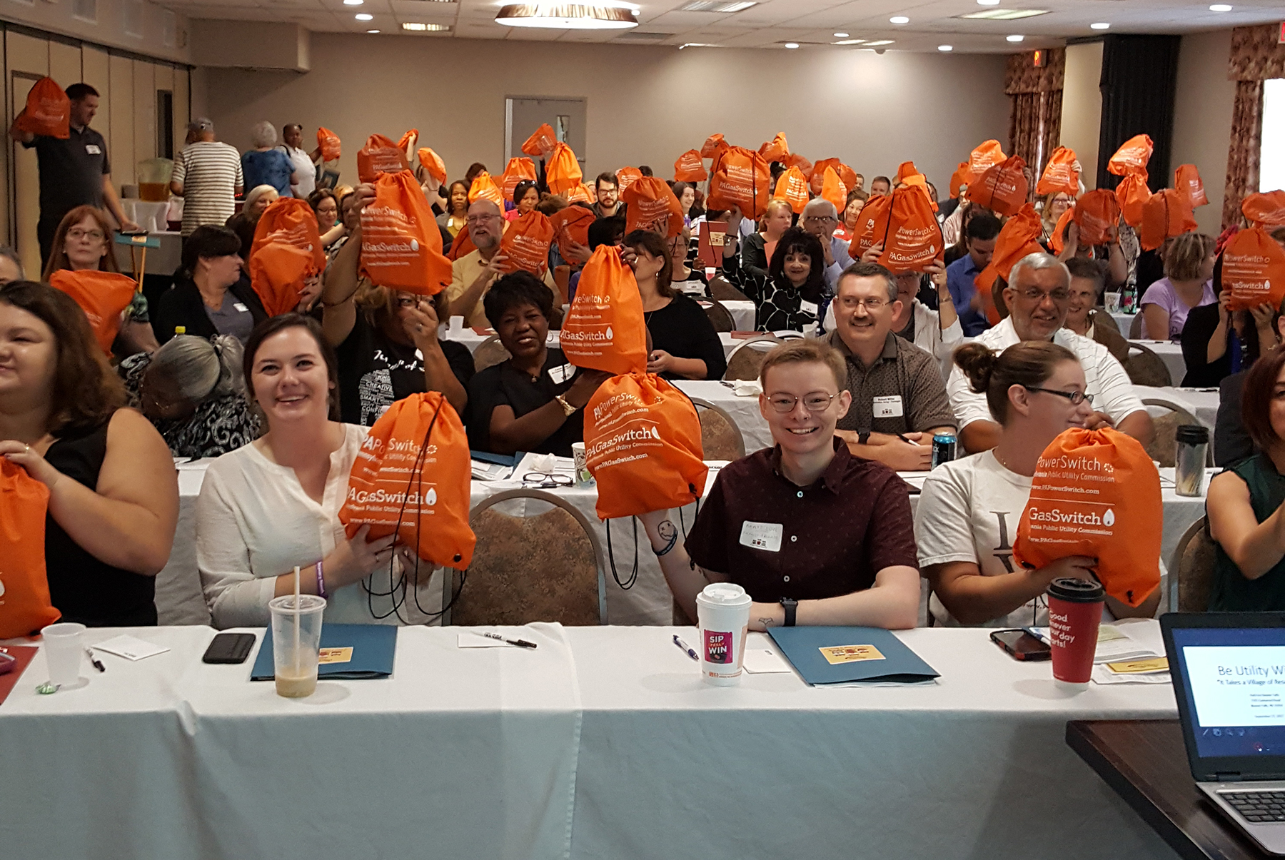 Event attendees hold up the orange bags given out by the PUC.