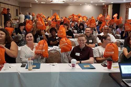 Event attendees hold up the orange bags given out by the PUC.